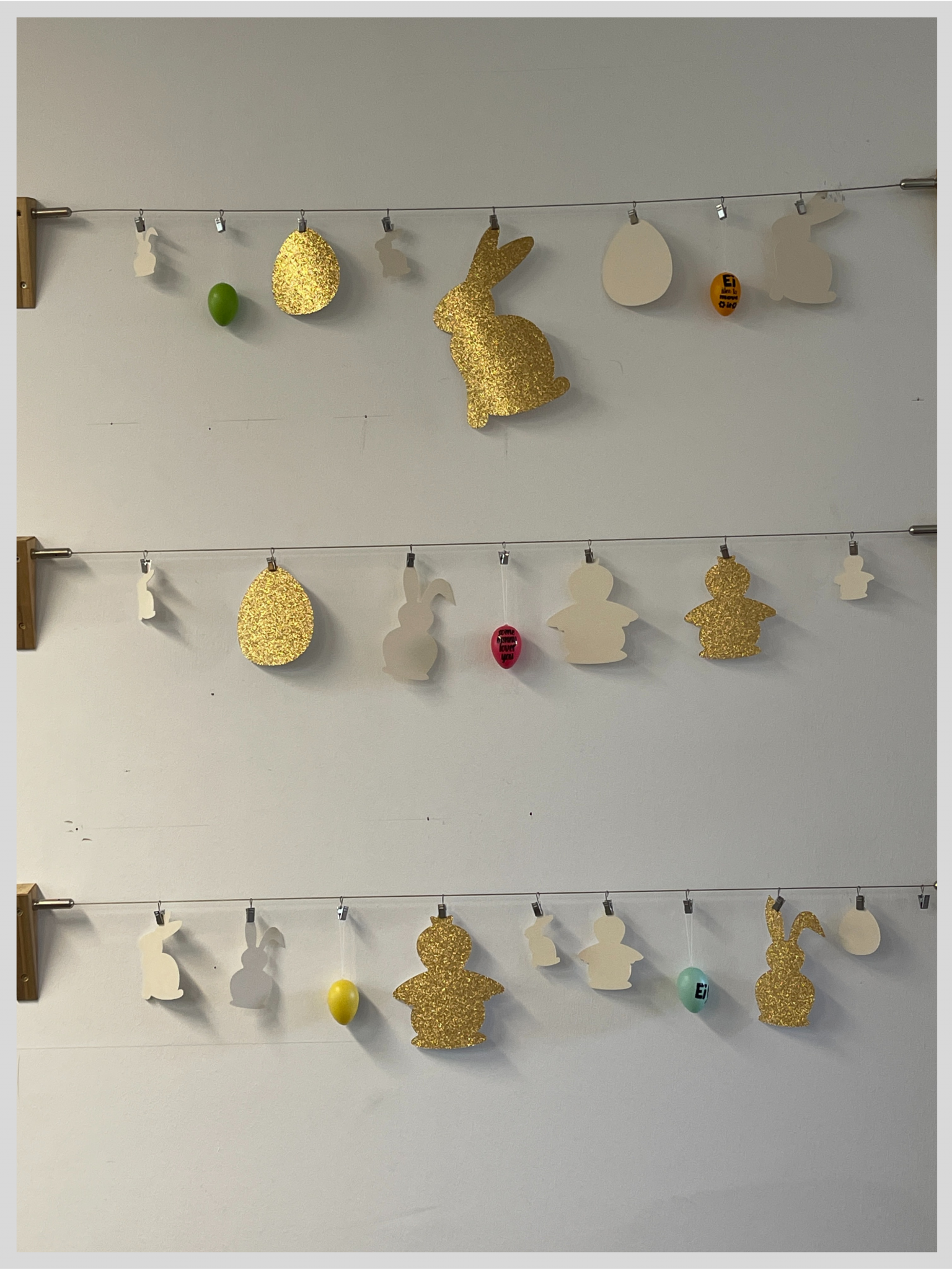 Osterdeko an drei Drahtseilen: mit Plotter geschnittene Hasen, Eier und Küken aus goldenem Glitzer- und weißem Papier, dazu bunte Ostereier