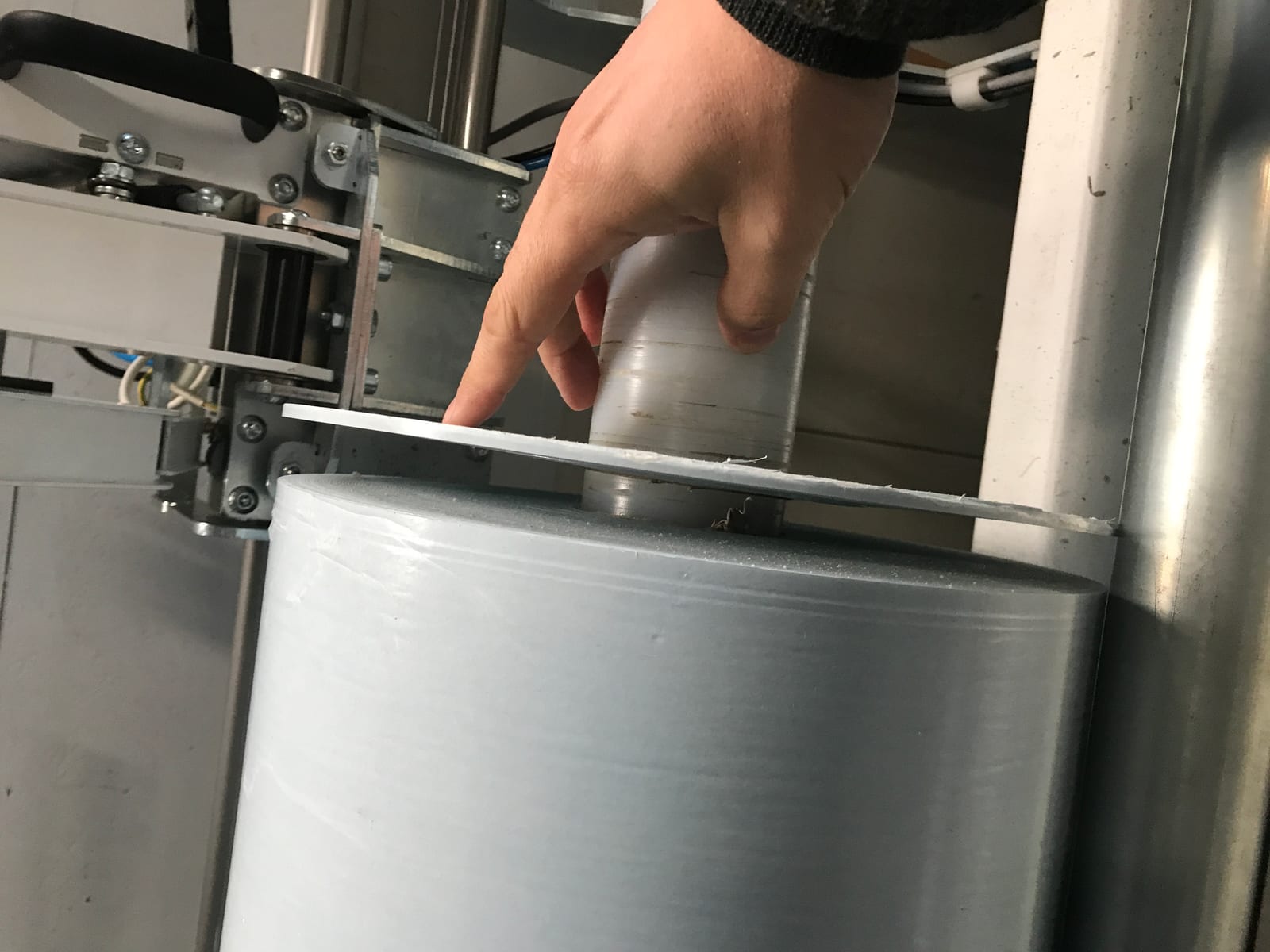 Finger zeigt auf frisch abgestochene Scheibe doppelseitigen Schaumklebebands auf großer Rolle in Abstechmaschine, Schnittkante leicht ausgefranst