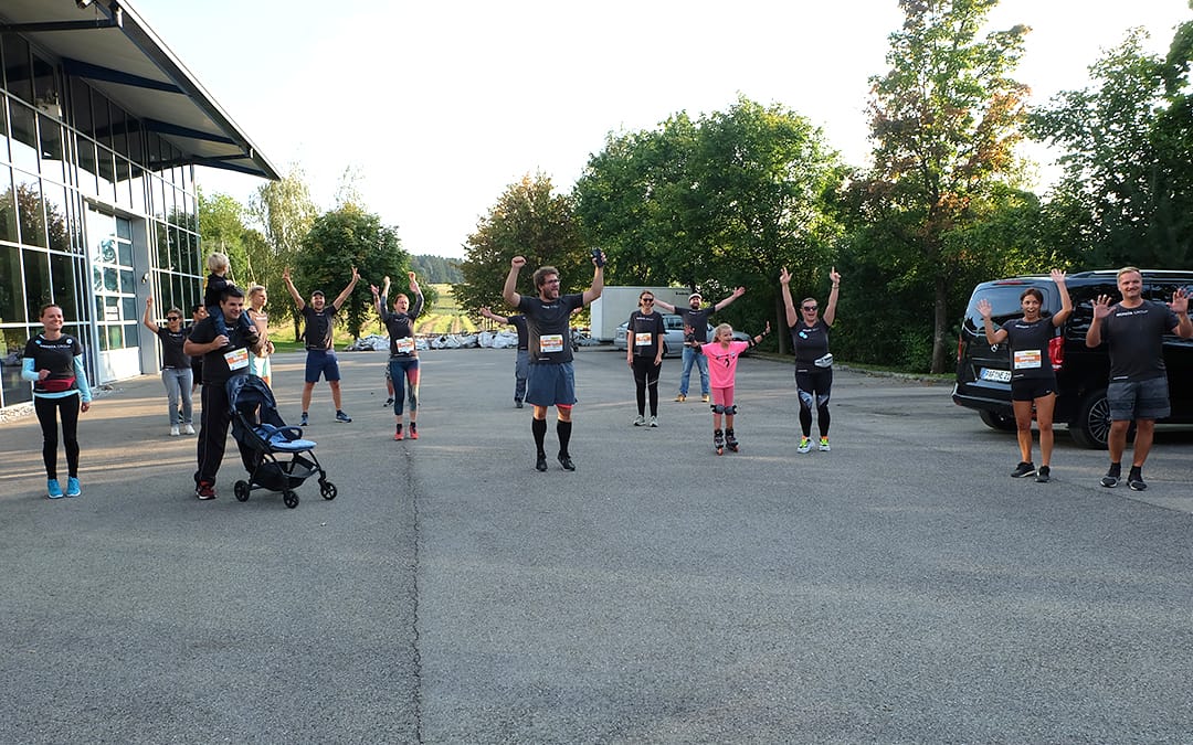The Nepata team, wearing dark running tops with race numbers, are cheering with their arms raised in a car park, spaced out, with a child on rollerblades