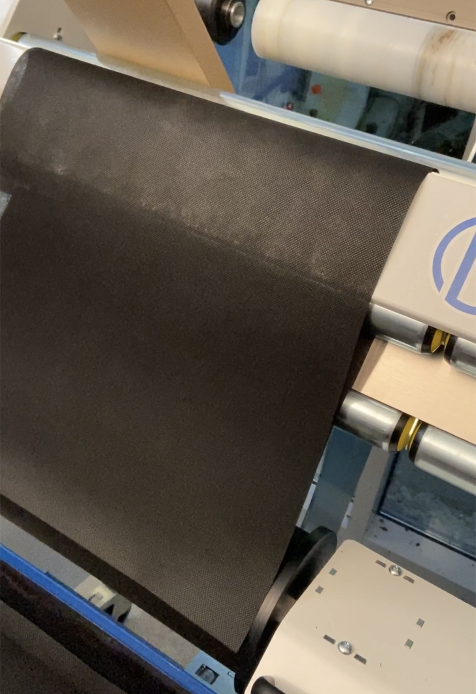 Schwarzer Vliesstoff für Gesichtsmasken läuft beim Umwickeln über die Walzen des NEPATA-Konvertierungs-Zentrums UA1650 ADWS