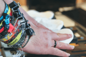 Hand mit zahlreichen bunten Festivalbändchen am Handgelenk greift nach weißen Gesichtsmasken, die auf einem Tisch liegen