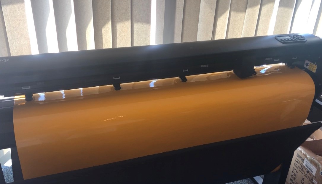 Schwarzer Schneideplotter mit eingespannter orangefarbener Selbstklebefolie, bereit zum Ausplotten des Bootsaufklebers
