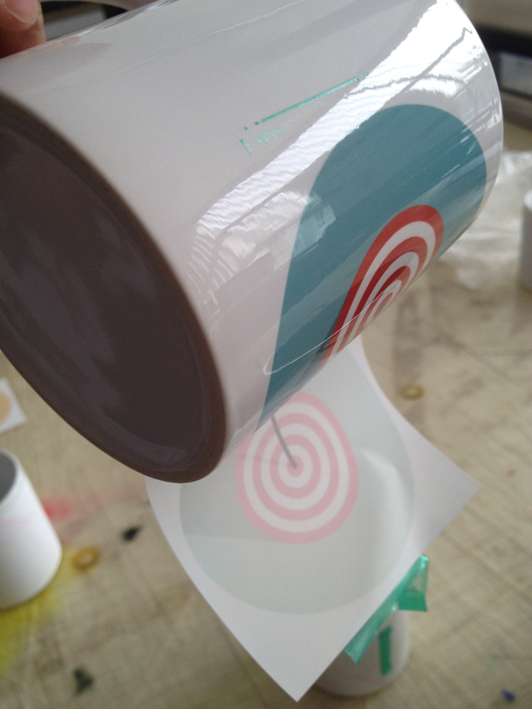 Transferpapier wird in einem Zug von heißer sublimierter Tasse abgezogen, darauf blaues Motiv mit roten Kreisen, Papier mit blassem Restabdruck