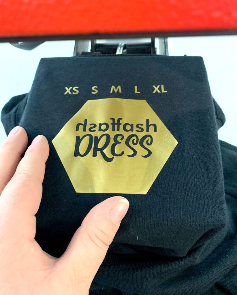 Goldenes Label mit Größenangaben XS bis XL und Hexagon-Logo auf schwarzem Shirt, gezielt gepresst auf der kleinen Heizplatte der Secabo TC1