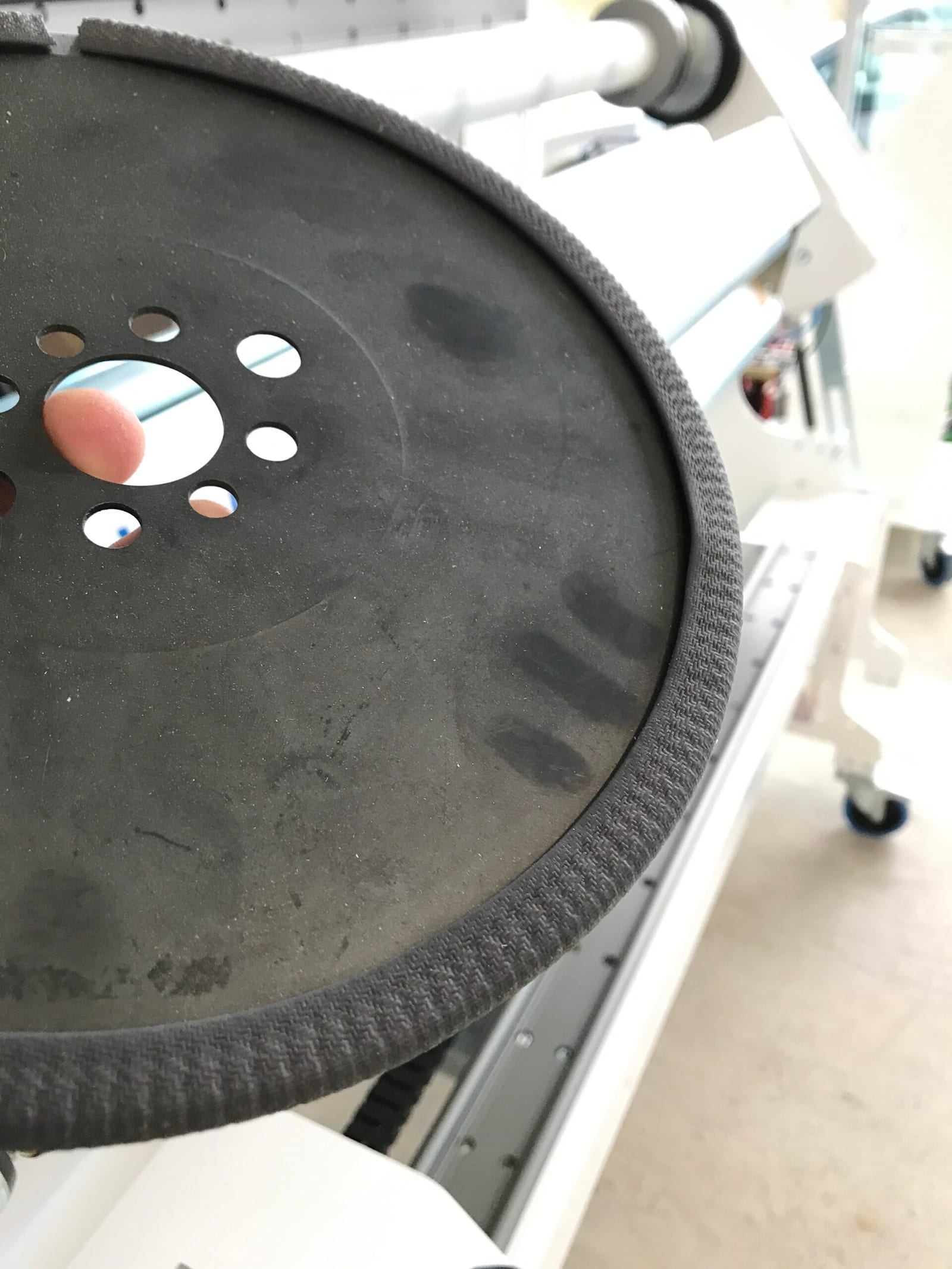 Runde Abstechklinge mit Lochmuster, Gebrauchsspuren und geriffelter Kante, in der Hand gehalten vor einer weißen Schneidemaschine