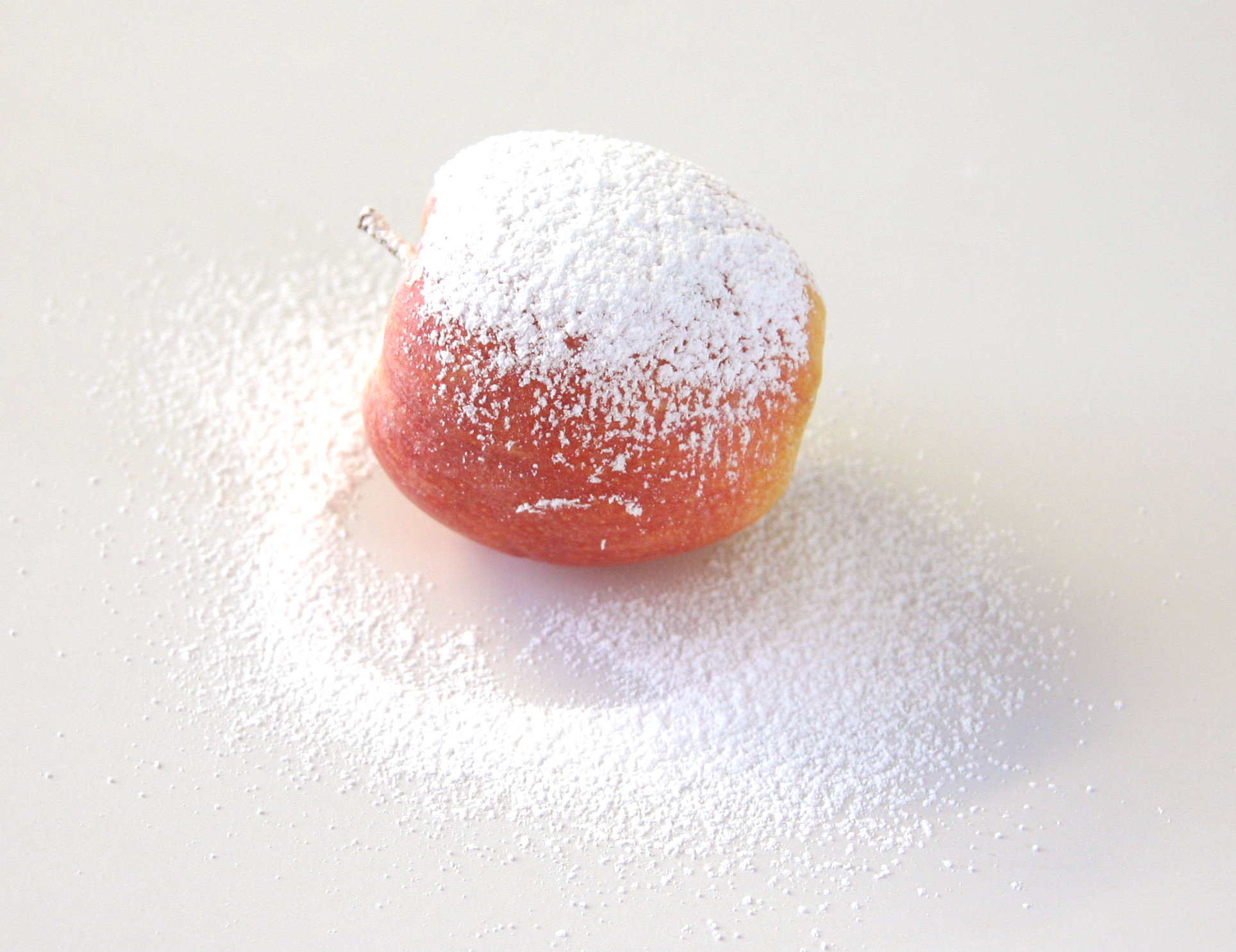 Roter Apfel, oben dicht mit Puderzucker bestäubt, auf weißem Untergrund mit verstreutem Zucker, Schritt 3 der Winteräpfel-Anleitung