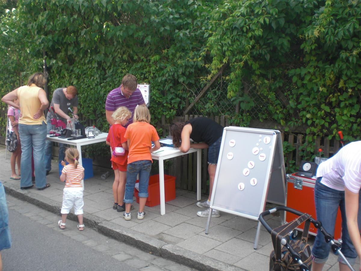 YOW!-Stand am Kindertag in Wolnzach: Kinder gestalten an Tischen mit Buttonmaschinen Buttons, daneben eine Tafel mit fertigen Buttons