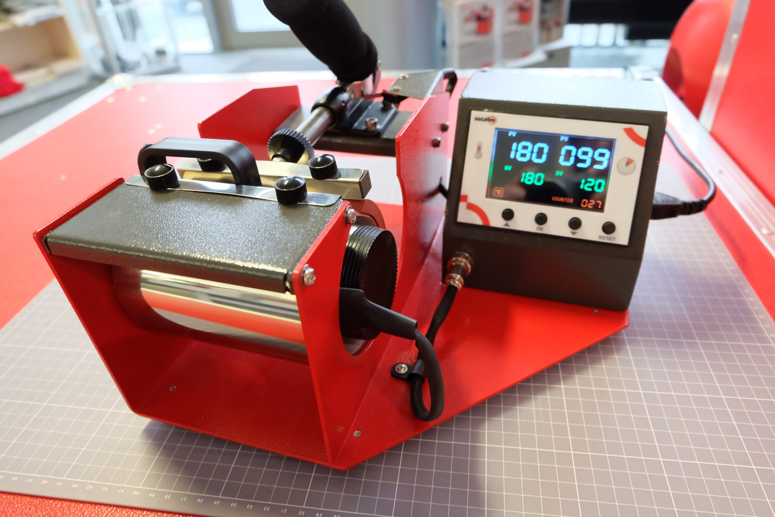 Edelstahl-Thermobecher in roter Secabo TM1 Tassenpresse, Display zeigt 180 °C und laufenden Timer bei 99 von 120 Sekunden