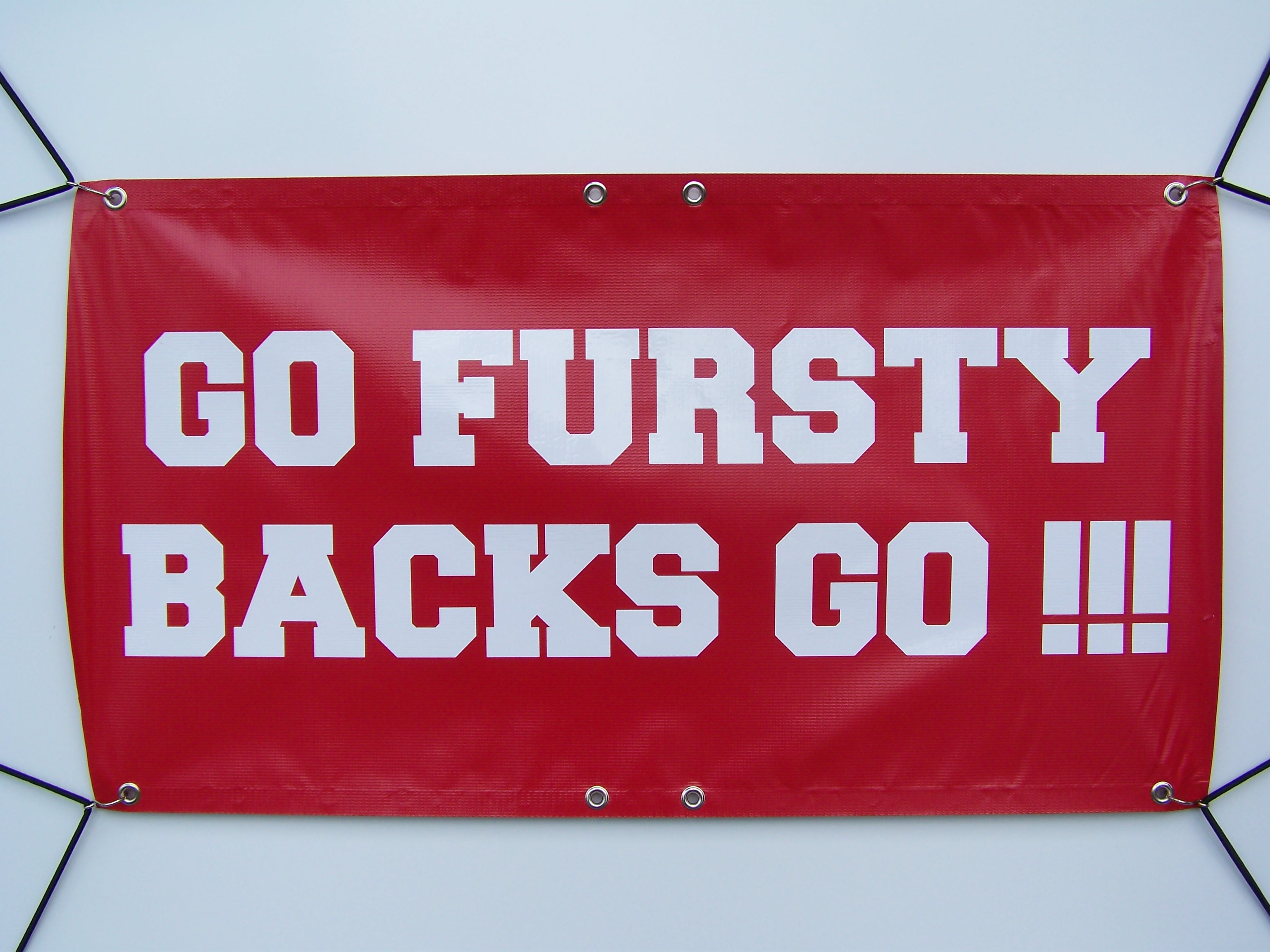 Rotes Banana Banner mit weißem Folienschriftzug GO FURSTY BACKS GO !!!, vorgesäumt und mit Metallösen, an Spannseilen befestigt