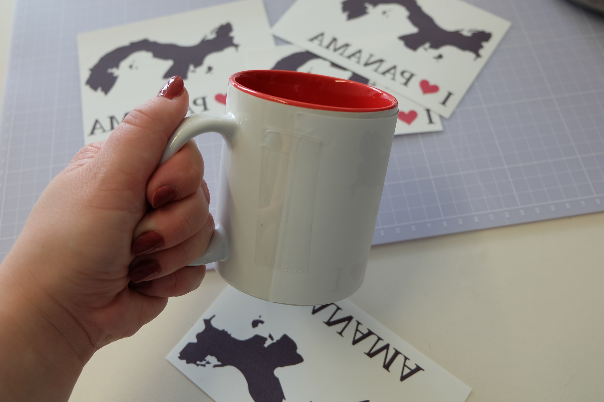Weiße Subli-Tasse mit roter Innenseite, Motiv mit hitzebeständigem Klebeband aufgeklebt; dahinter gespiegelte I-love-Panama-Drucke