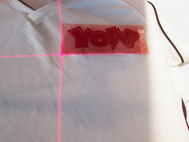 Rote Kreuzlaserlinien auf weißem Funktionsshirt, YOW!-Transfer mit der unteren linken Ecke exakt am Kreuzungspunkt ausgerichtet