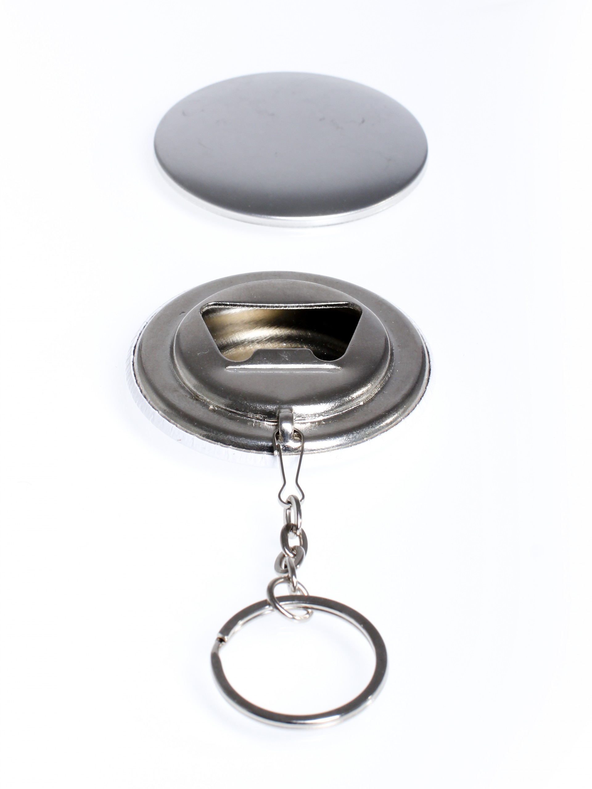 Buttonrohling mit Flaschenöffner-Rückseite und Schlüsselring an Kette, dahinter das unbedruckte Metall-Oberteil, auf weißem Grund